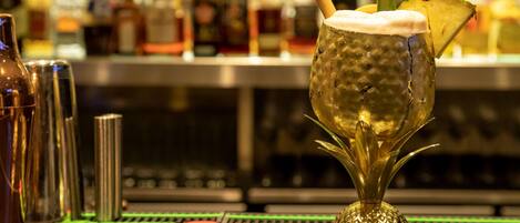 A bar setting with a drink in a decorative glass, bar tools, and a blurred background of bottles.