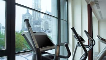 An indoor gym with stationary bikes and a large window overlooking a historic building.