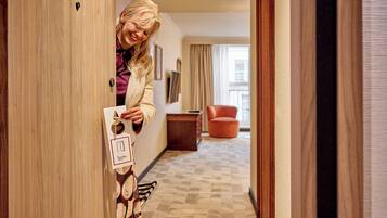 Ein Hotelzimmer-Eingangsbereich mit Holztür, einer Kärtenspendung und einem gemusterten Teppich. Im Hintergrund steht ein roter Stuhl.