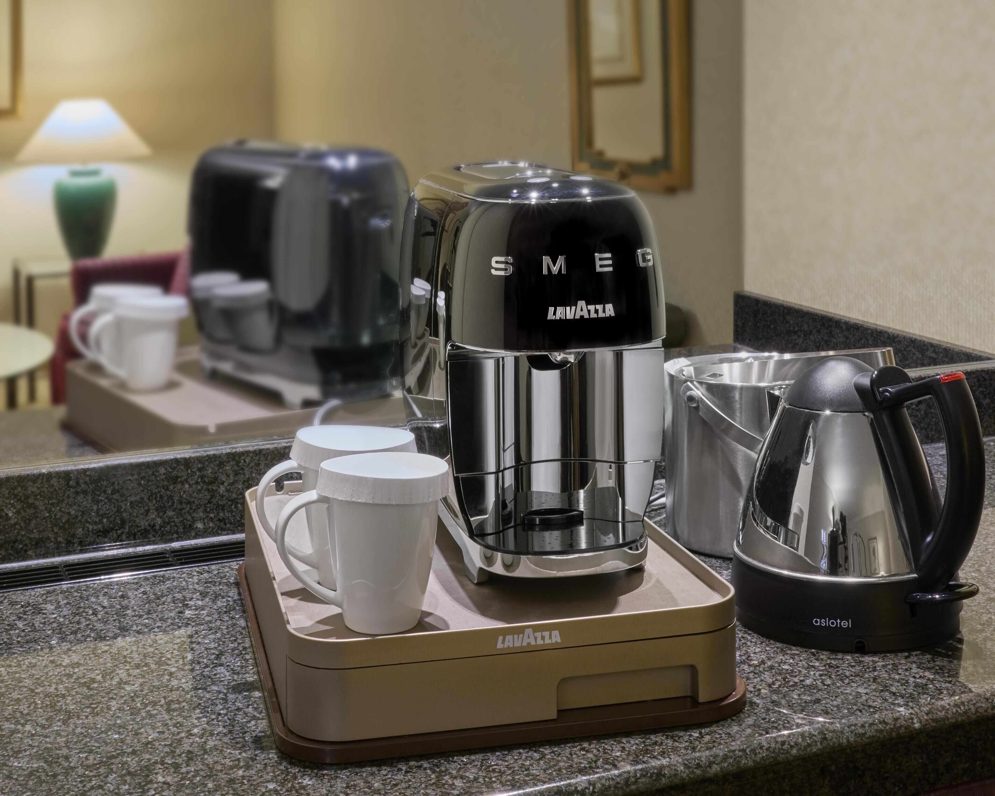 A coffee station with a coffee maker, a kettle, and two mugs on a countertop.