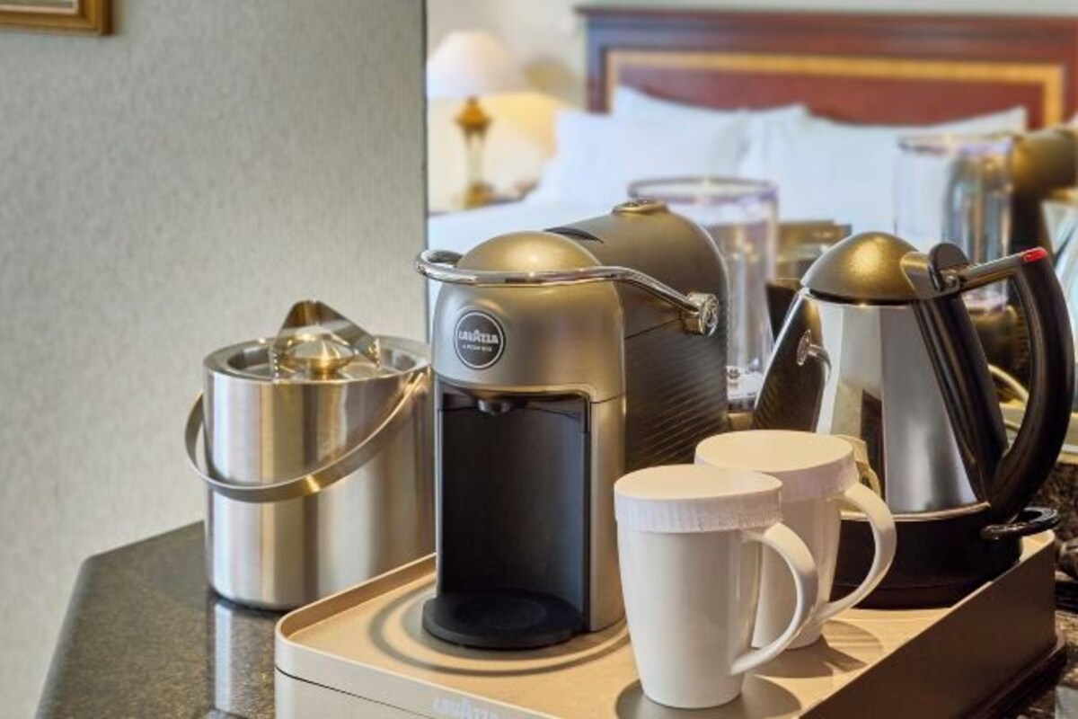 A coffee station with a coffee maker, a milk frother, and two white mugs on a tray.