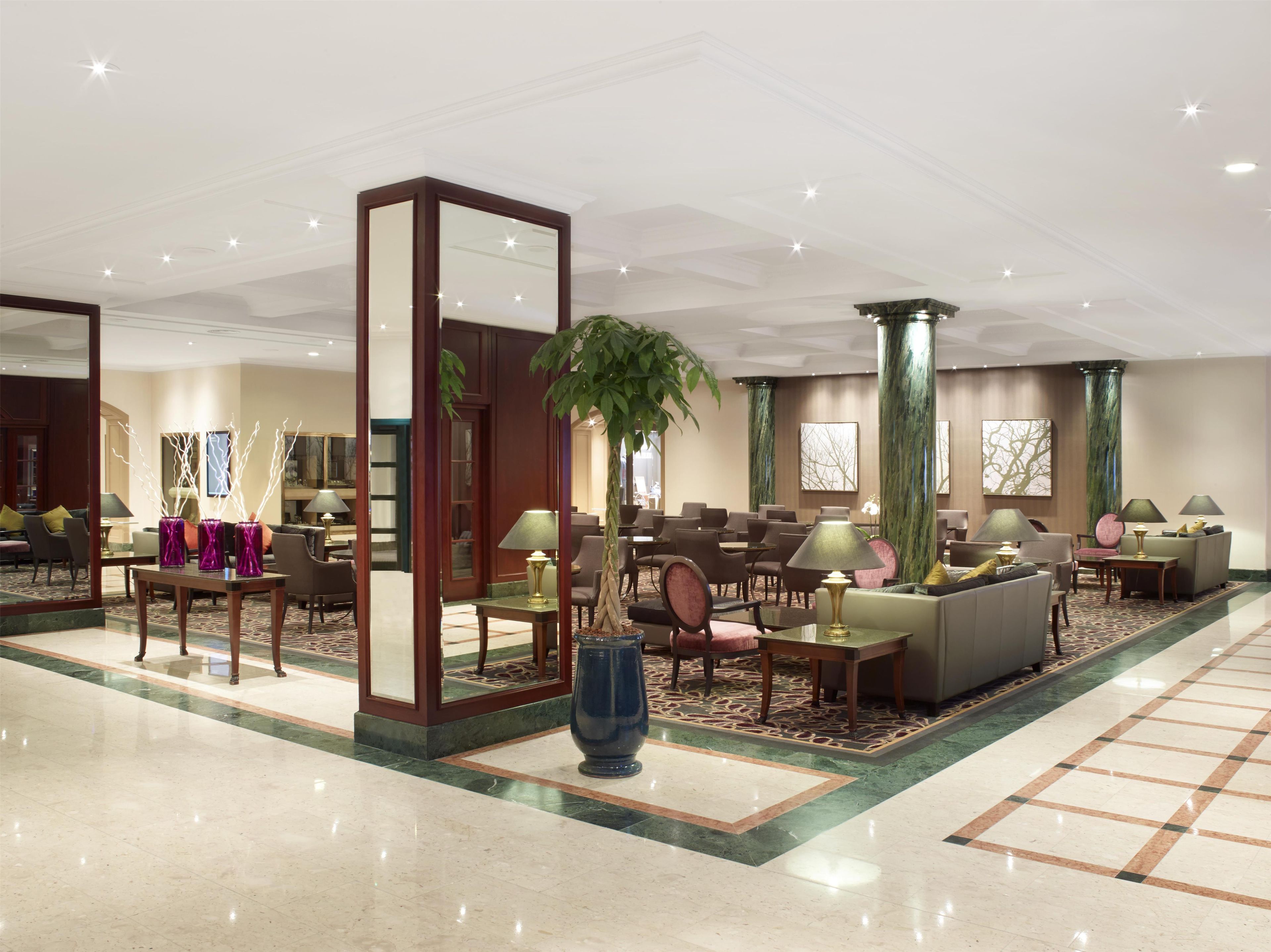A hotel lobby with a seating area, a large mirror, and a decorative vase.
