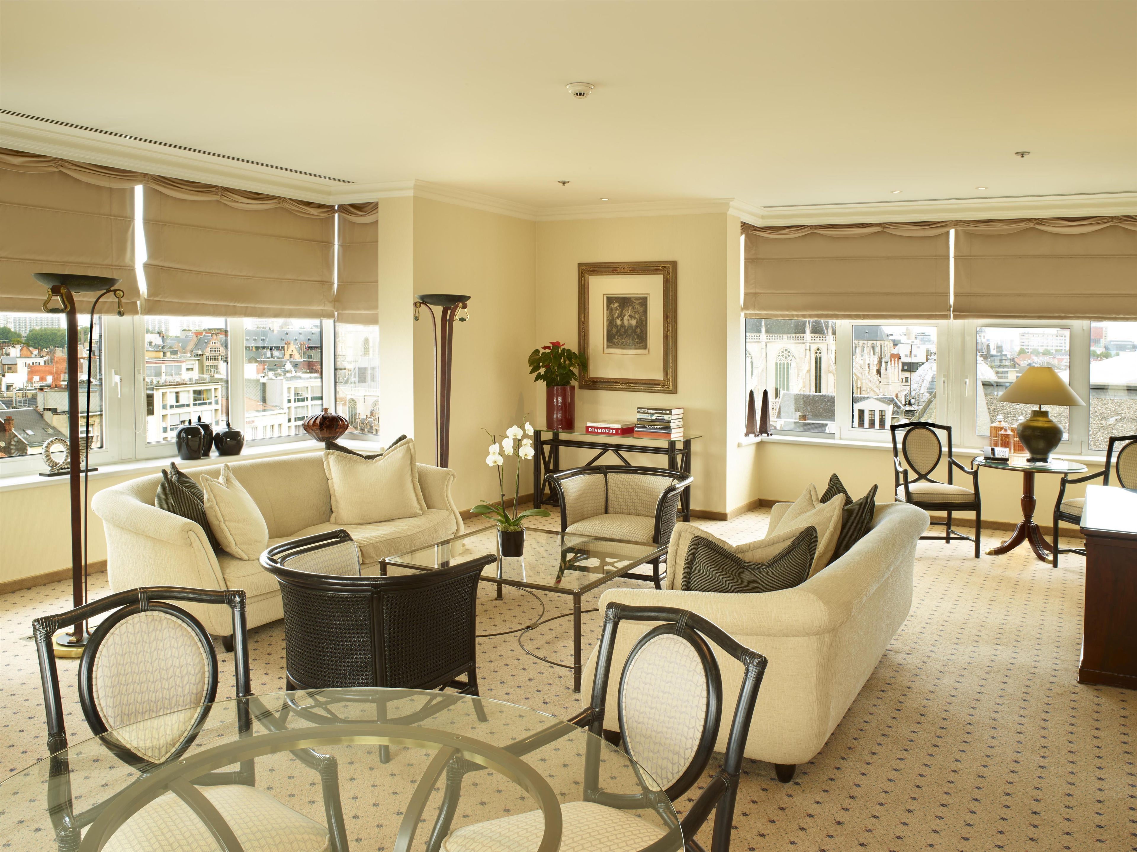 A spacious living area with a sofa, chairs, a glass coffee table, and a view of the city through large windows.