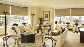 A spacious living area with a sofa, chairs, a glass coffee table, and a view of the city through large windows.