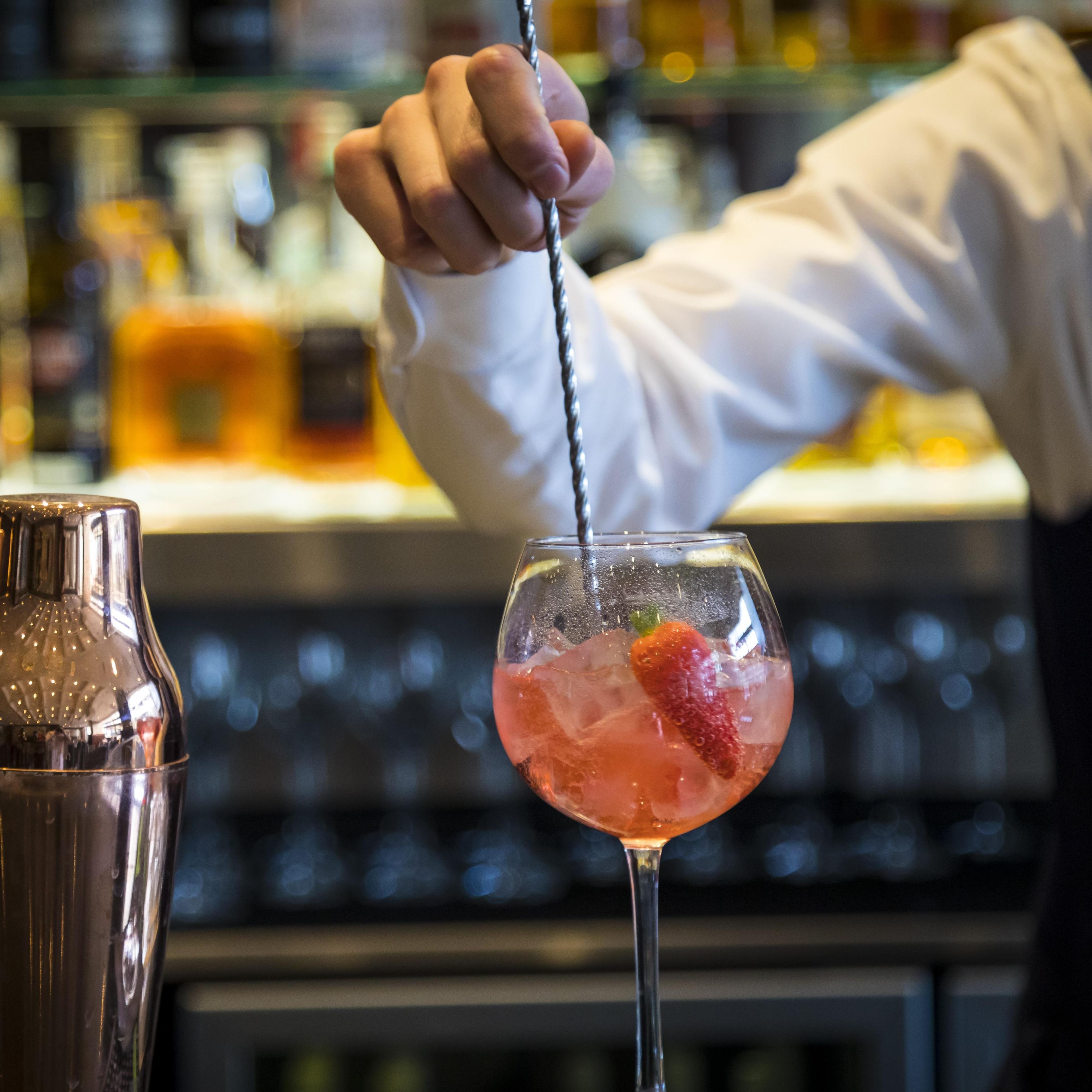 A bartender pouring a drink into a glass with ice and a strawberry.