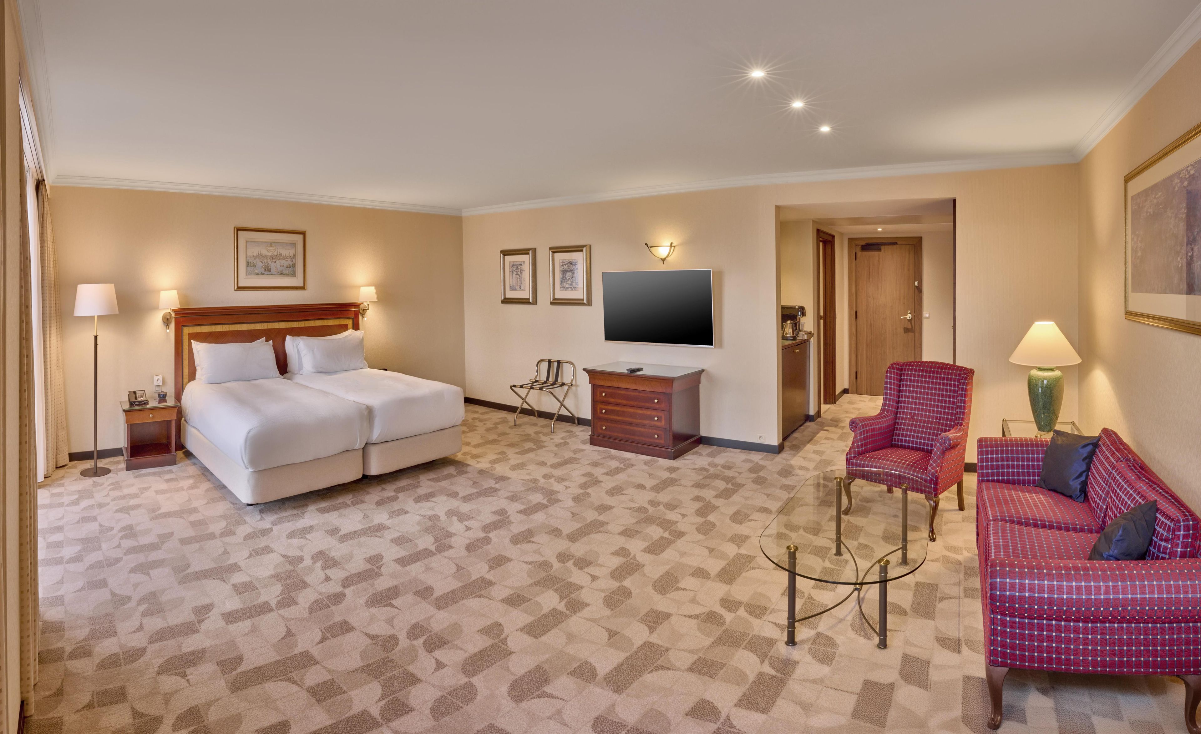 Een hotelkamer met een tweepersoonsbed, een televisie, een bureau, een stoel en een bank.