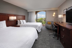 A hotel room with two beds, a desk, a chair, a TV, and a balcony with a view.