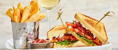 A plate with a grilled sandwich, a glass of white wine, and a container of fries.