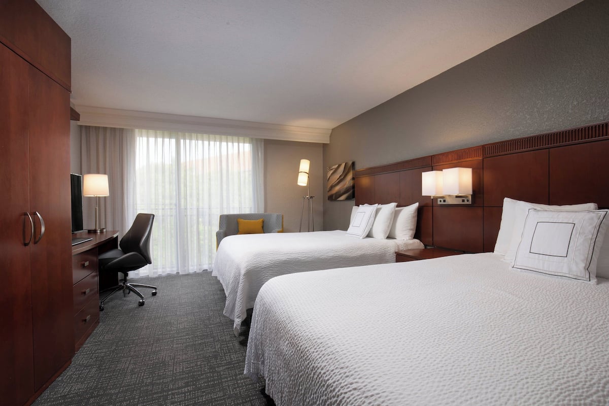 Una habitación de hotel con dos camas, un escritorio, una silla y un televisor.