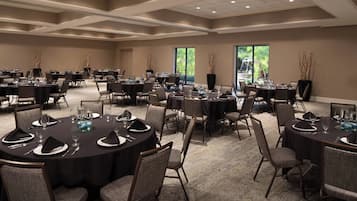 Une grande salle de conférence équipée de plusieurs tables rondes, chacune agrémentée d’assiettes, de couverts et de verres.
