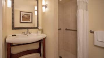 A bathroom with a sink, mirror, framed artwork, shower with curtain, and towel rack.