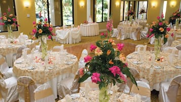 Un salón de banquetes con mesas redondas dispuestas para un evento formal, con centros de mesa florales y manteles blancos.