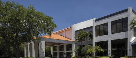 A modern building with a covered entrance, large windows, and a landscaped garden with trees and shrubs.