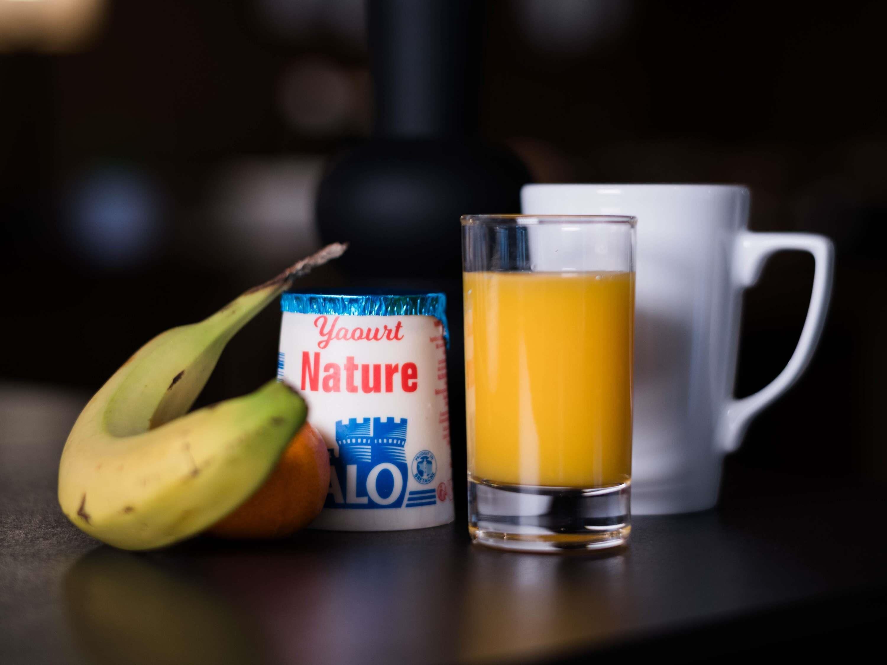 Un verre de jus d’orange, une tasse blanche et un pot de yaourt.