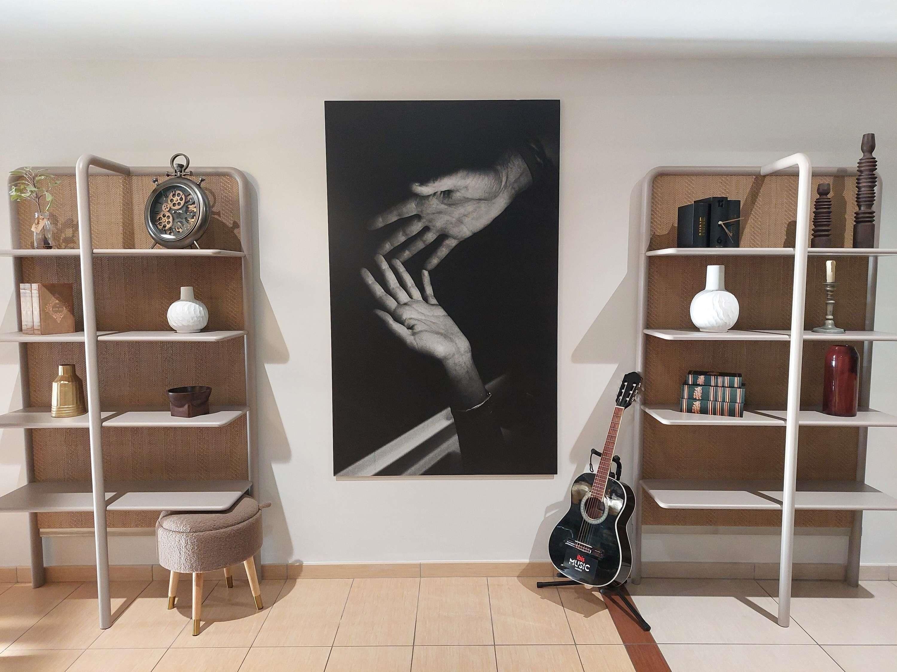 Una habitación con dos estanterías blancas, una guitarra negra y una fotografía grande en blanco y negro en la pared.