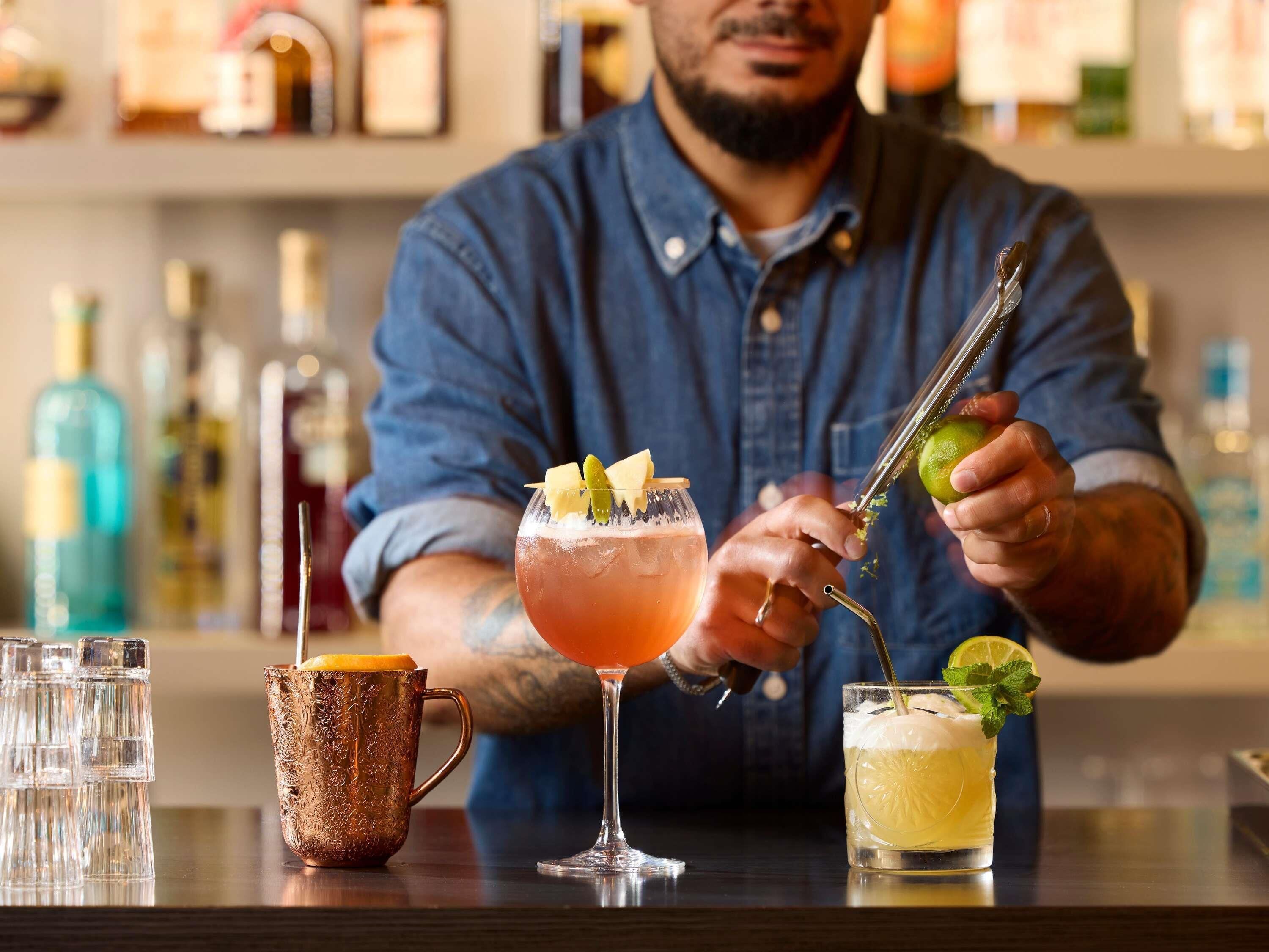 A bartender preparing drinks with a variety of bottles in the background.