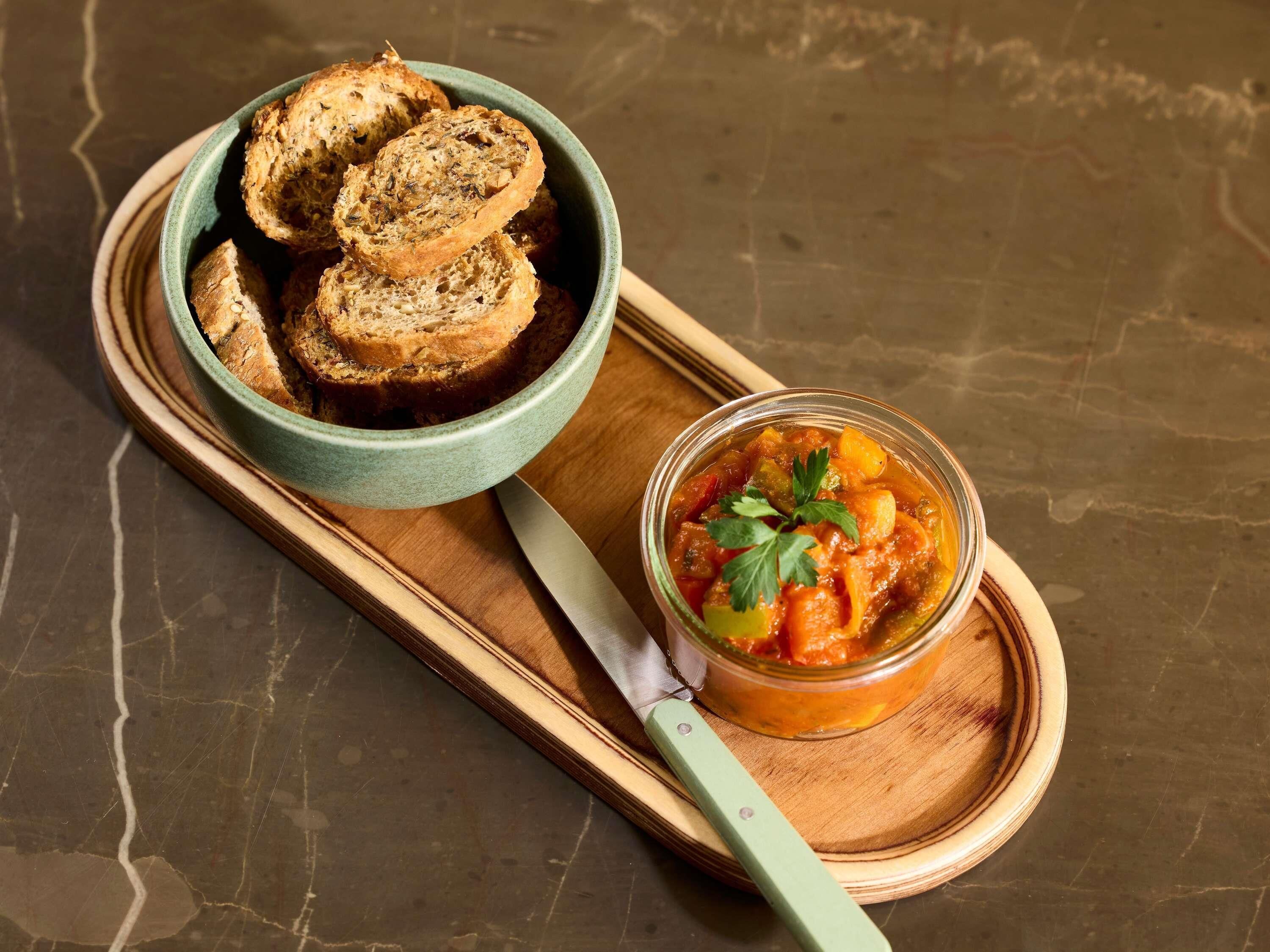 A bowl of sliced bread and a jar of tomato-based condiment on a wooden board.