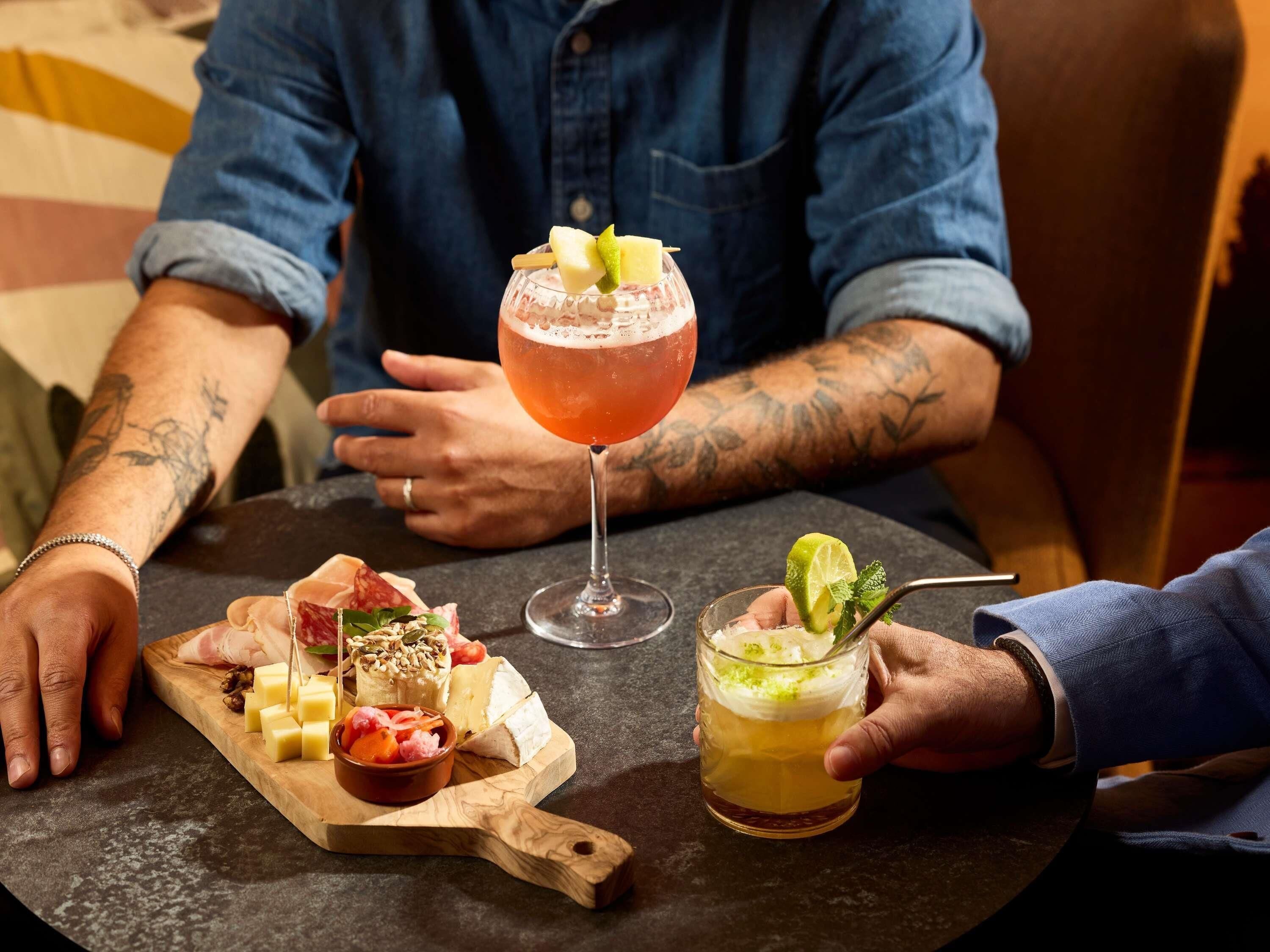 A table with a variety of cheeses, cured meats, and a cocktail glass.