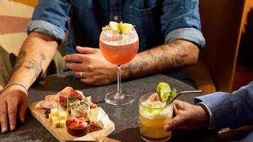 Uma mesa com diversos queijos, embutidos e uma taça de cocktail.