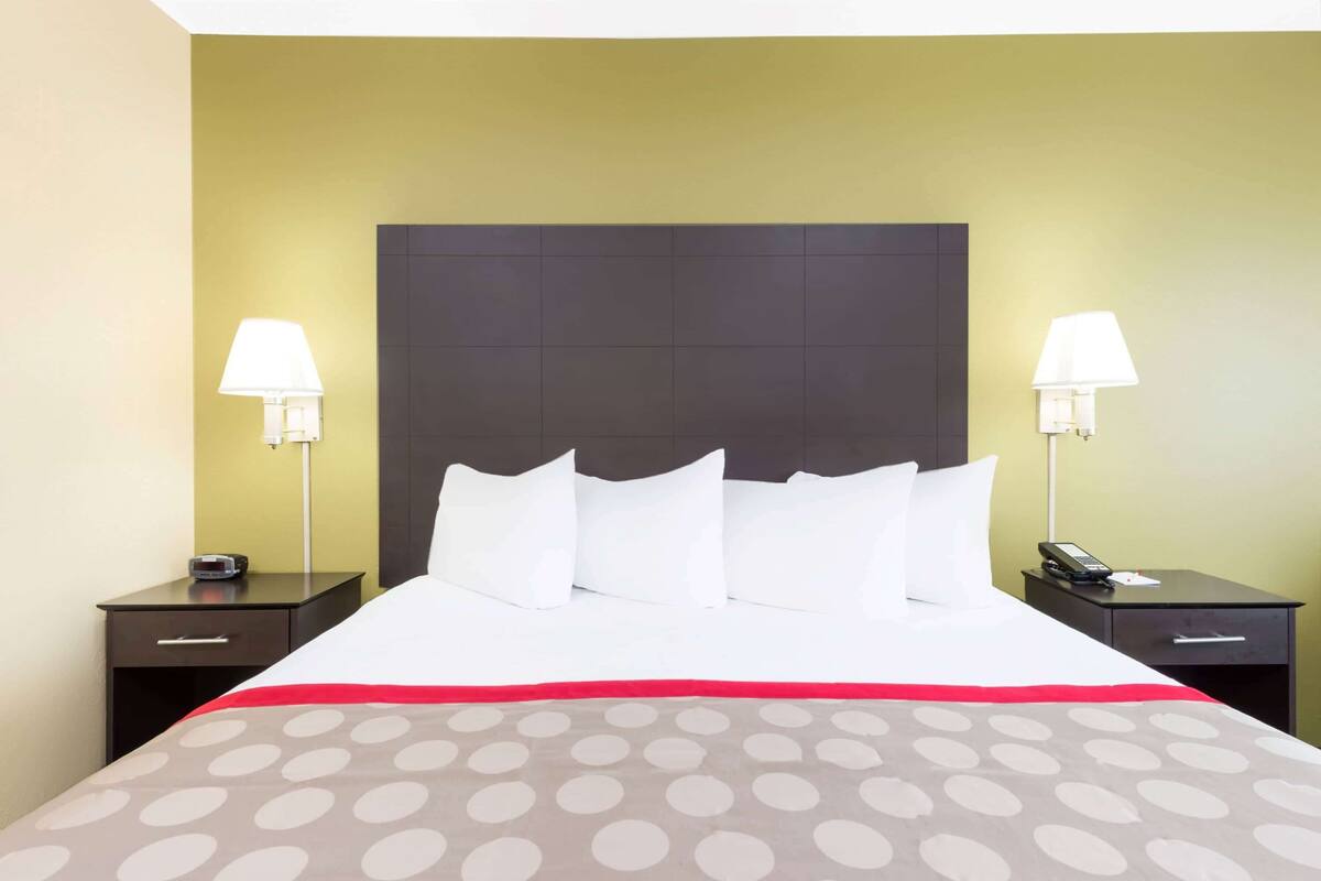 A hotel room with a large bed, two bedside tables, a nightstand, and a lamp on each side.