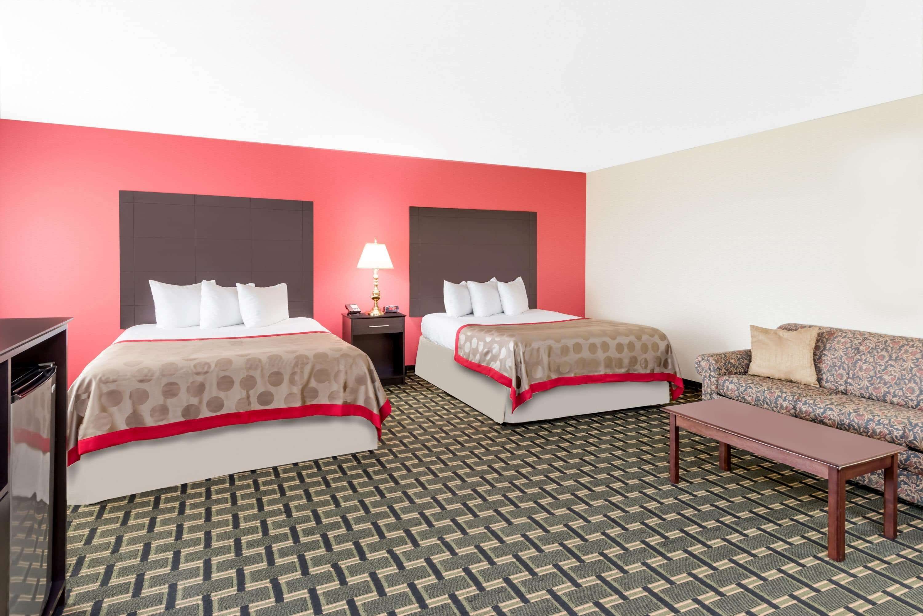 A hotel room with two beds, a sofa, a nightstand with a lamp, and a patterned carpet.