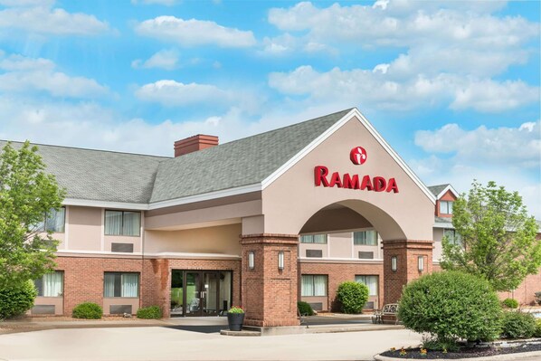A Ramada hotel with a brick facade, large entrance, and a clear sky.