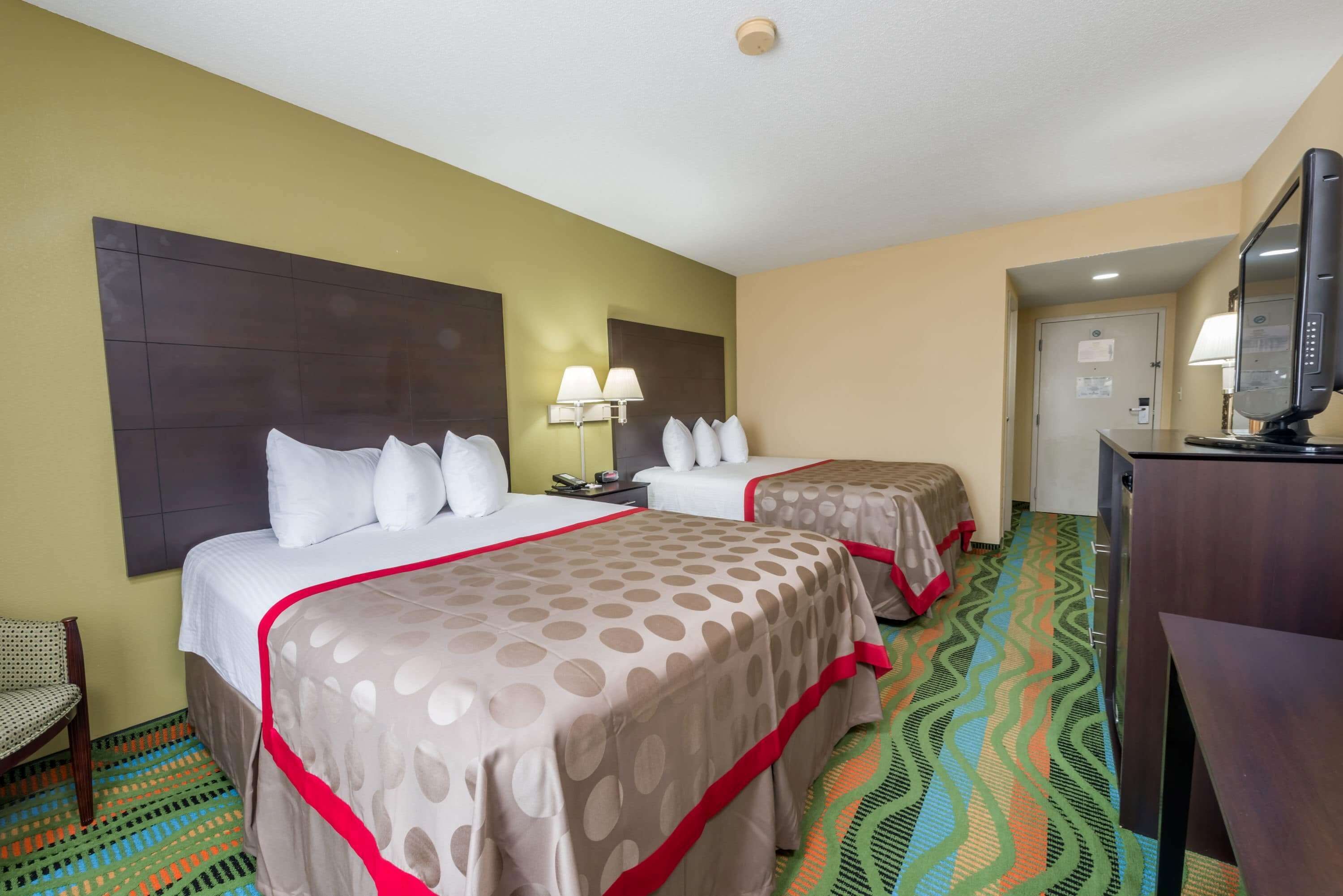 A hotel room with two beds, a desk, a chair, and a television.