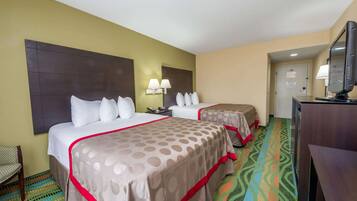 A hotel room with two beds, a desk, a chair, and a television.