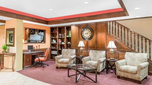 A lobby with a wooden staircase, a desk with a computer, and patterned armchairs.