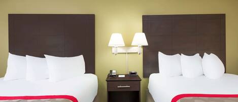 A hotel room with two beds, a nightstand with lamps, and a patterned rug.