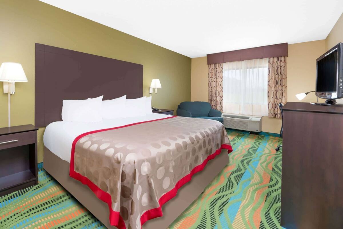 A hotel room with a bed, a desk, a chair, a TV, and a window with curtains.