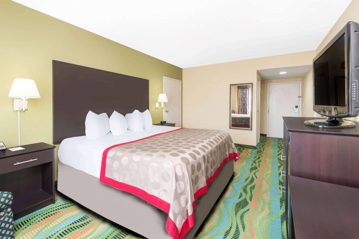 A hotel room with a bed, bedside tables, a television, and a patterned carpet.
