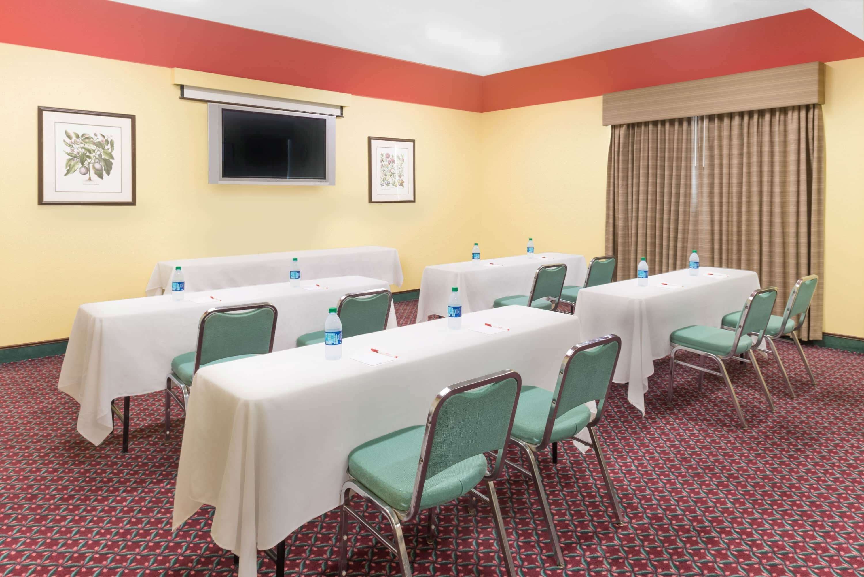 A conference room with multiple tables and chairs, framed pictures on the walls, and a large window with curtains.