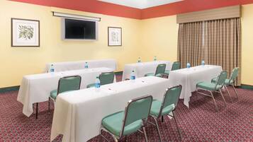 A conference room with multiple tables and chairs, framed pictures on the walls, and a large window with curtains.
