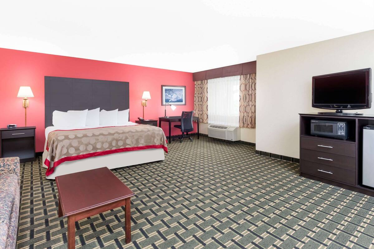 A hotel room with a bed, a desk, a TV, a microwave, and a window with curtains.