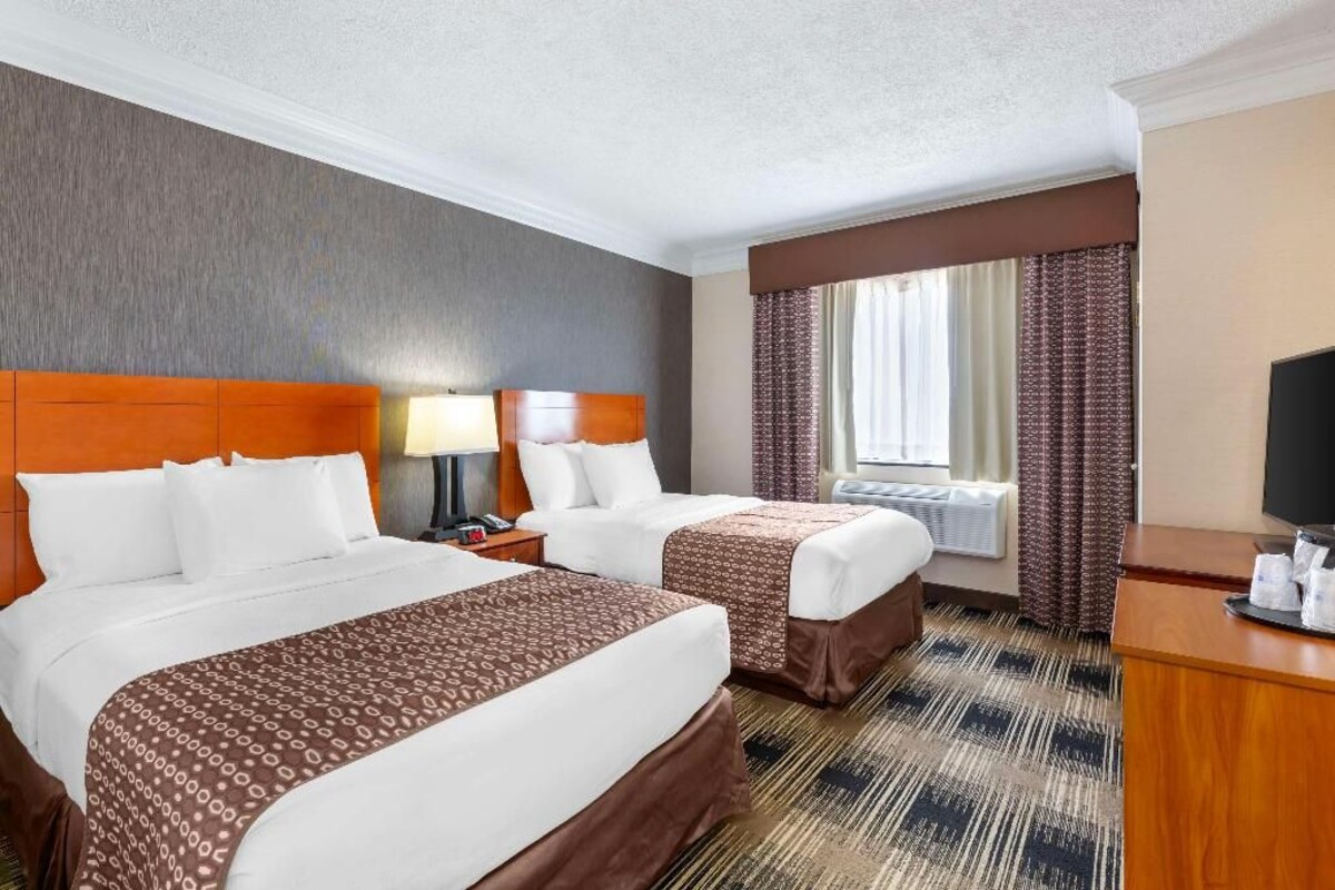 A hotel room with two beds, a desk, a television, and a window with curtains.