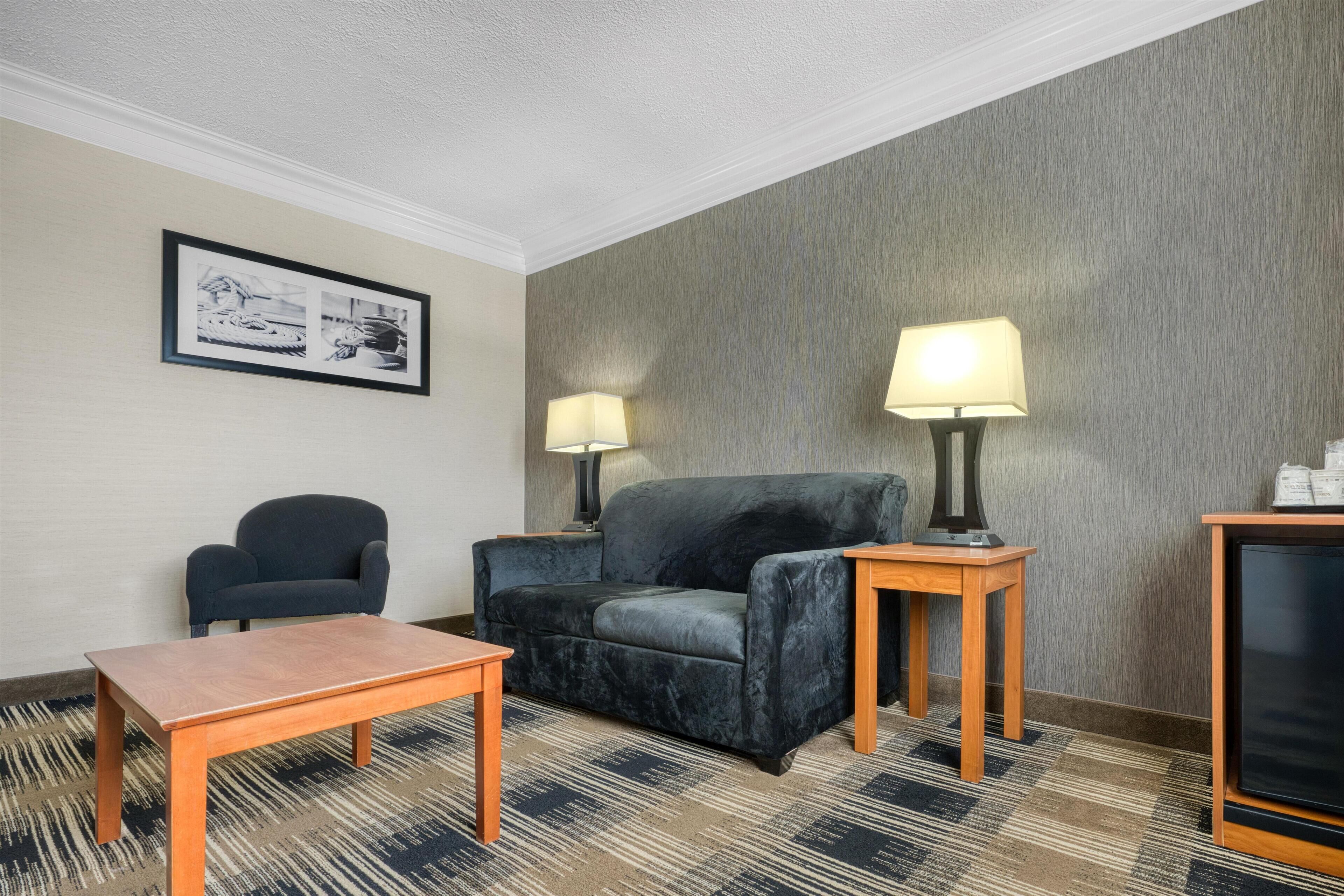 Une chambre d’hôtel avec un canapé, un fauteuil, une table en bois, deux lampes et un tableau encadré au mur.