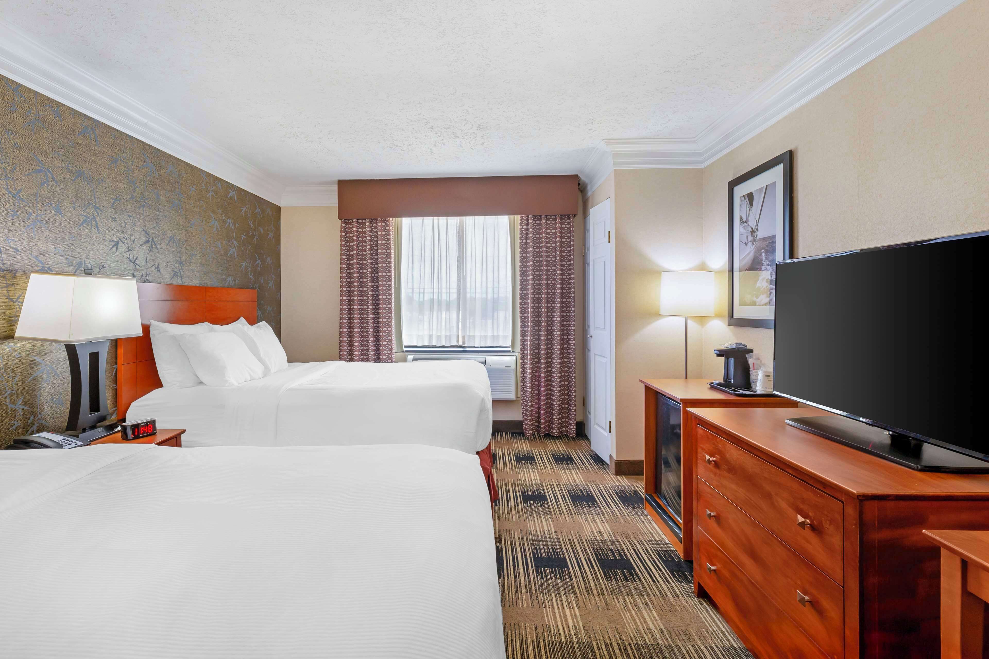 A hotel room with two beds, a television, a desk, and a window with curtains.