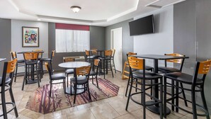 A dining area with round tables and chairs, a flat-screen TV mounted on the wall, and a framed picture on the wall.