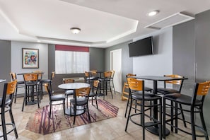 A dining area with round tables and chairs, a flat-screen TV mounted on the wall, and a framed picture on the wall.