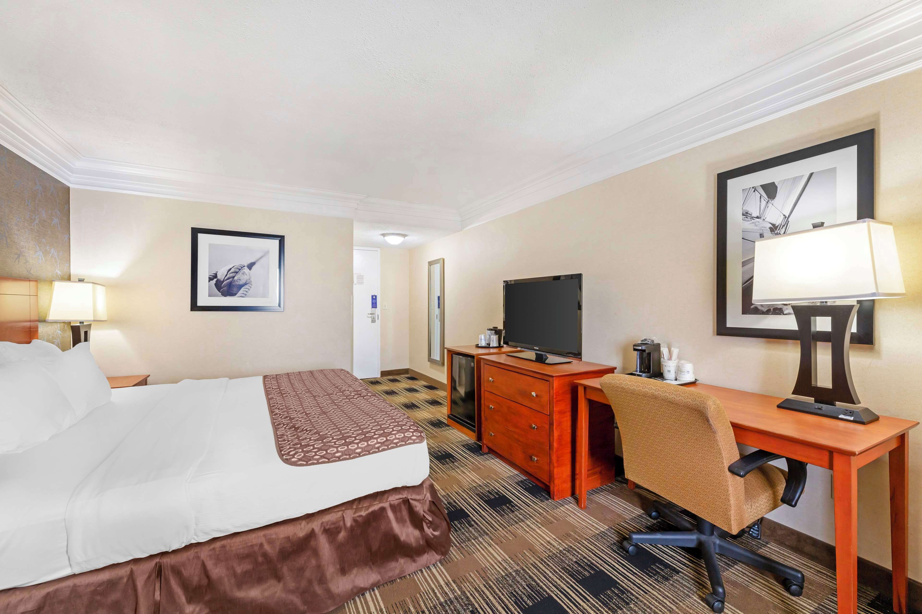 A hotel room with a bed, desk, chair, television, and artwork on the walls.