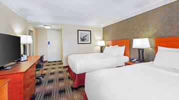 A hotel room with two beds, a desk with a TV, and a bathroom door.