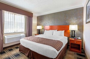 Una habitación de hotel con una cama grande, dos mesitas de noche con lámparas, un ventanal con cortinas y una pared con motivos de bambú.