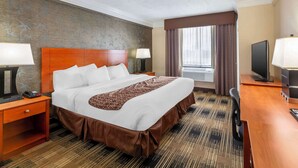 A hotel room with a large bed, two bedside tables with lamps, a television, and a window with curtains.