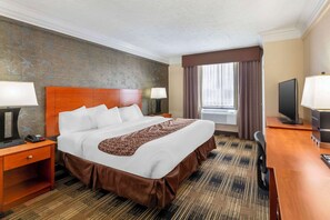 A hotel room with a large bed, two bedside tables with lamps, a television, and a window with curtains.