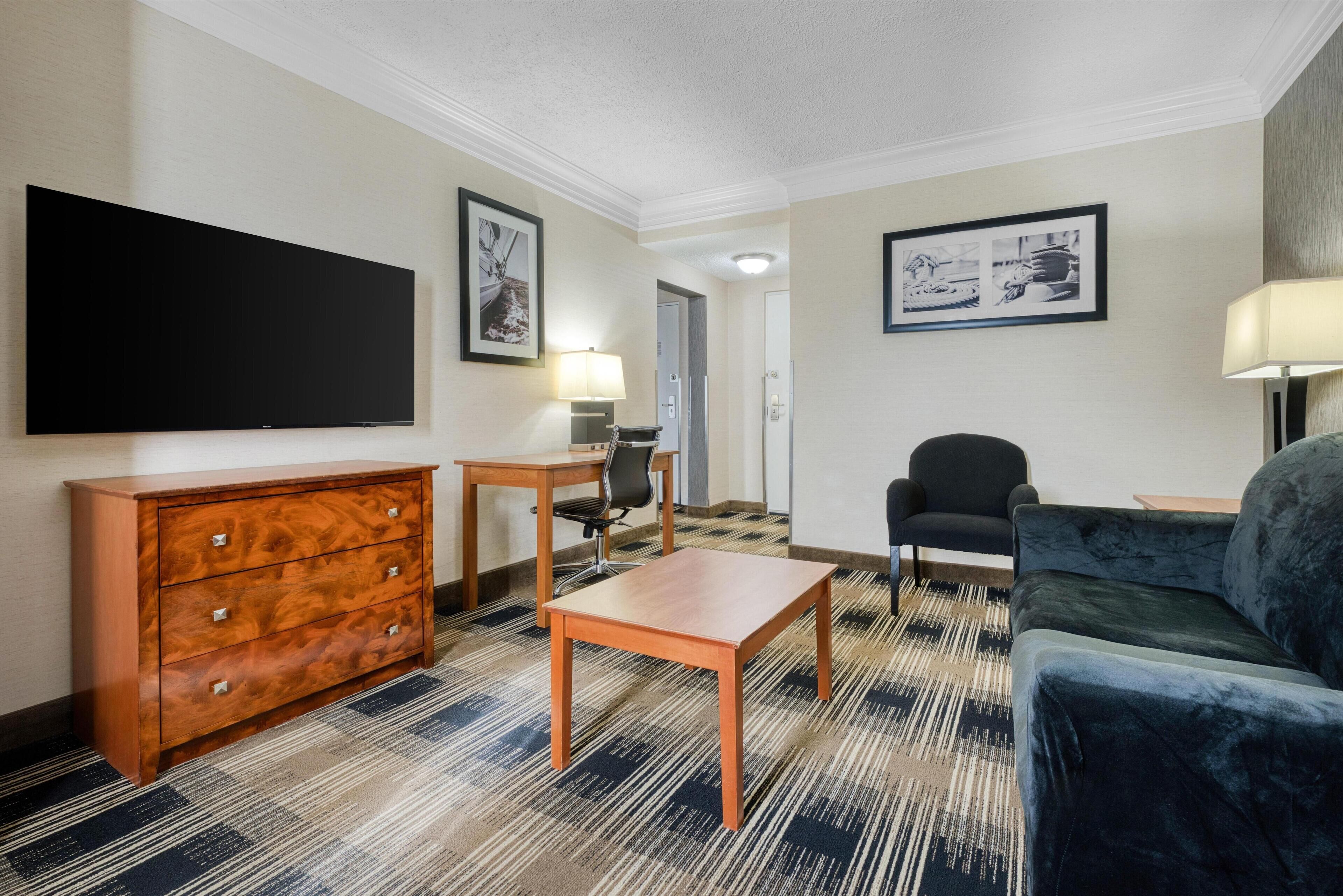 Habitación de hotel con televisión de pantalla plana, cómoda de madera, una mesita pequeña, un sofá azul y dos cuadros enmarcados en las paredes.