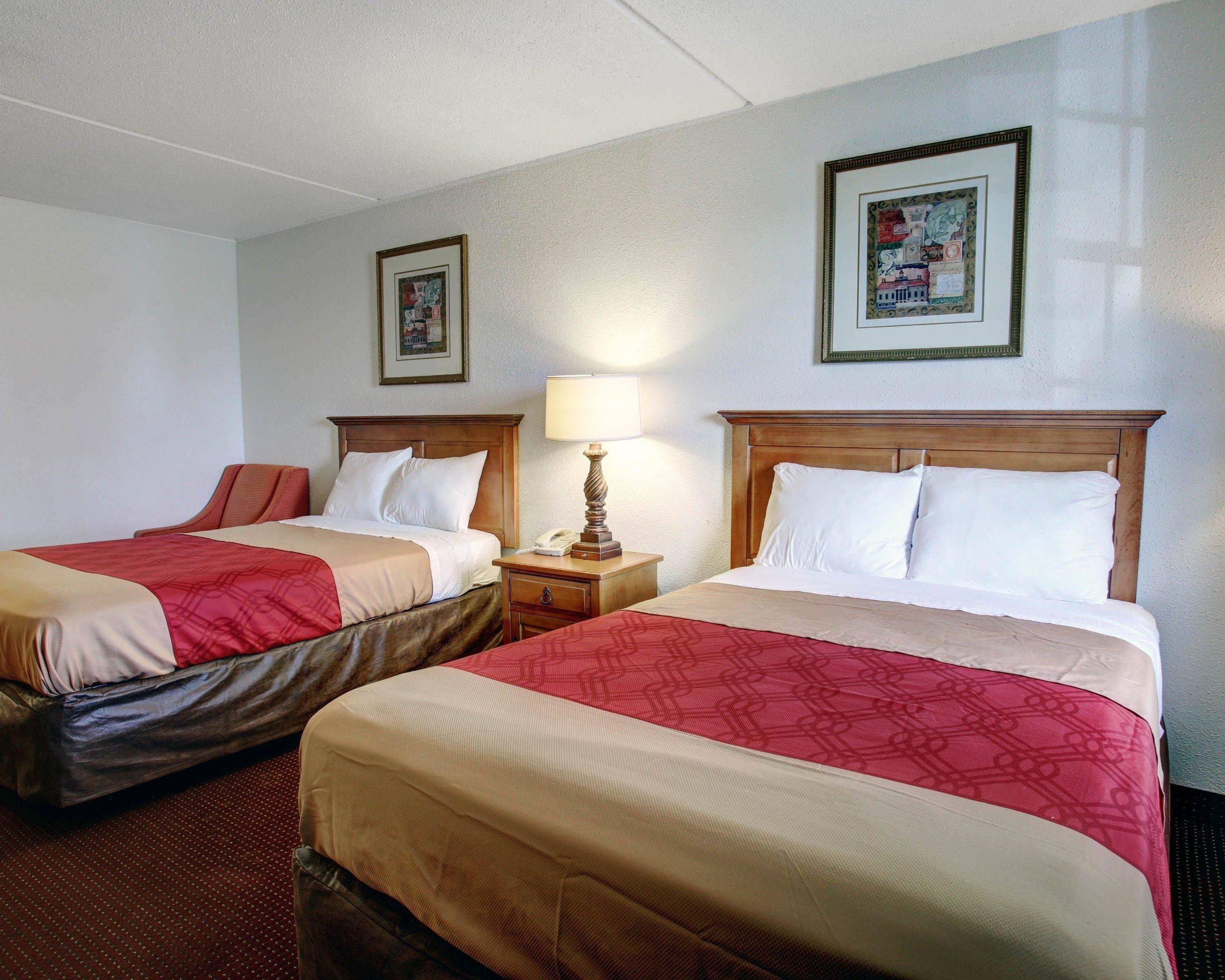 Habitación de hotel con dos camas, cada una con cabecero de madera, una mesita de noche con lámpara y un cuadro en la pared.