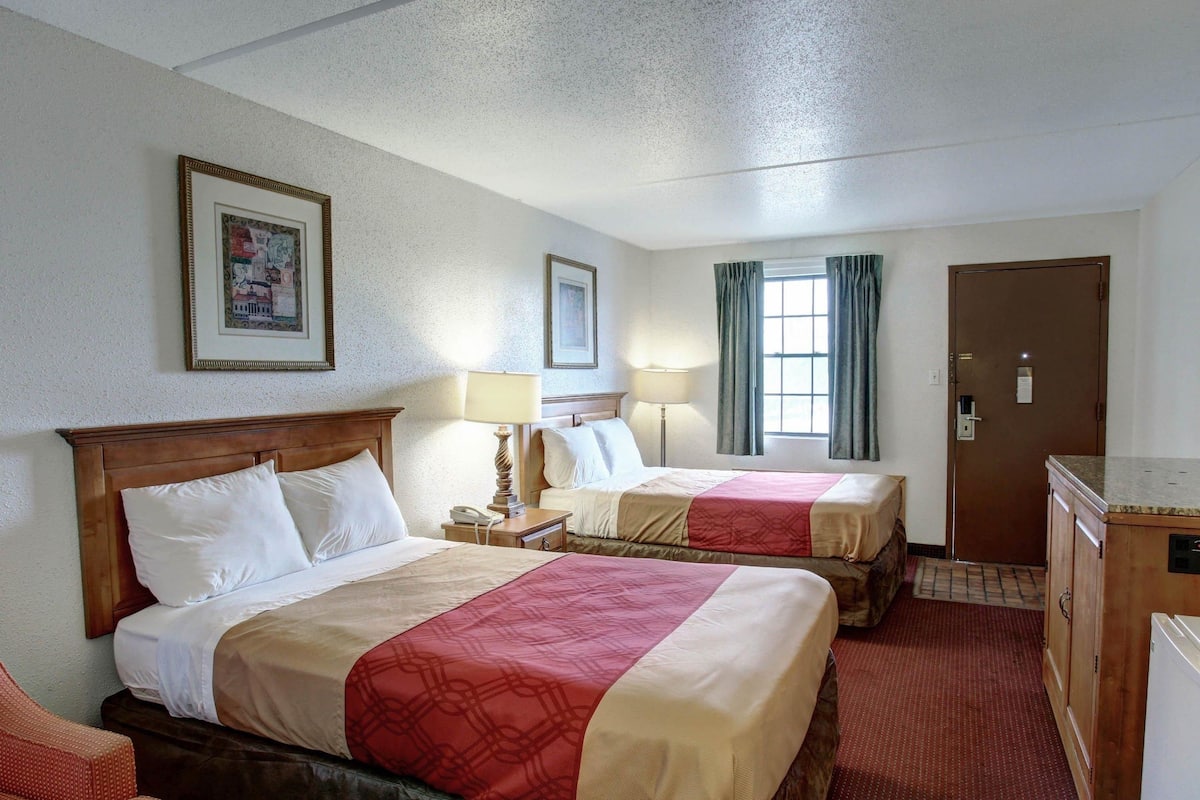 A hotel room with two beds, a desk, a chair, a dresser, and a window with curtains.