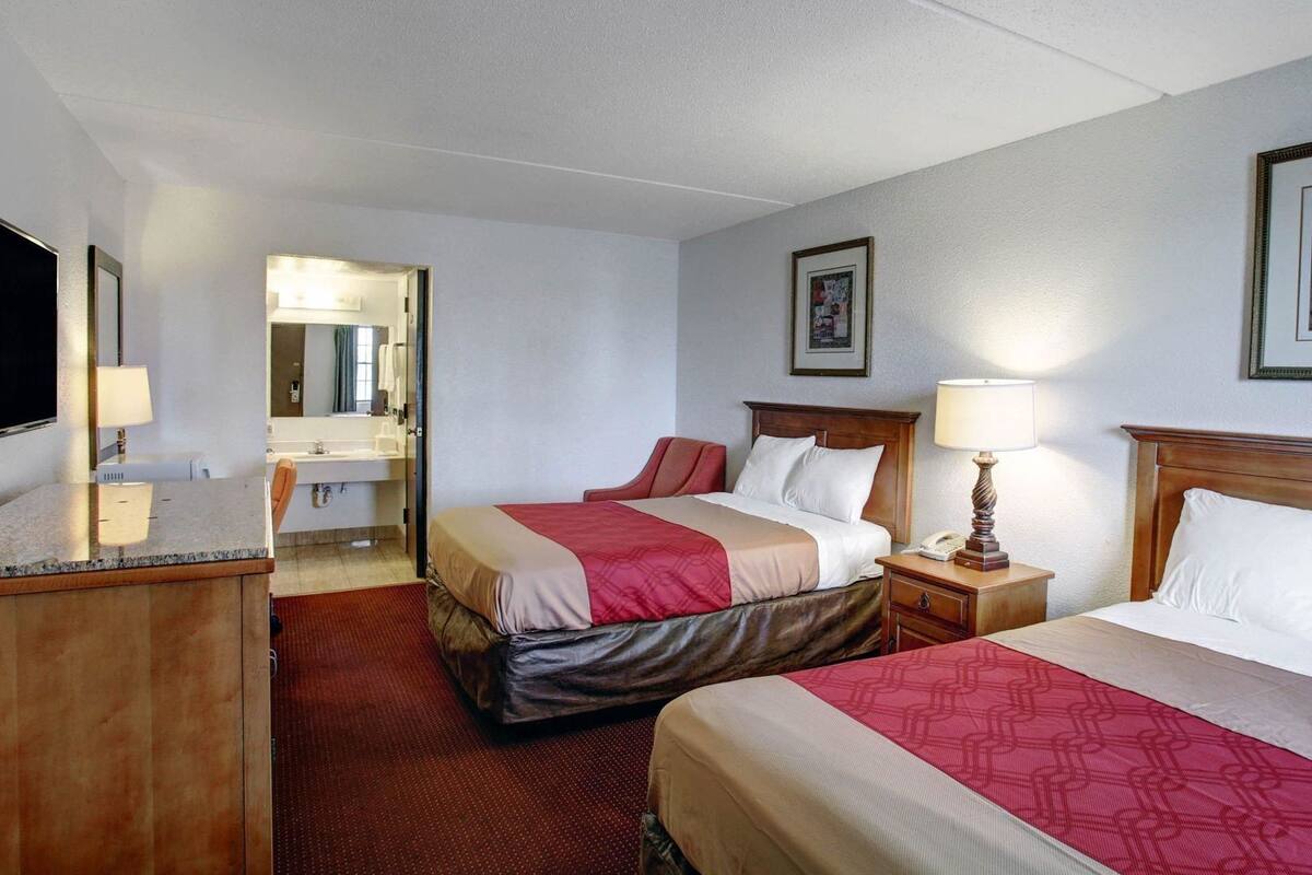 A hotel room with two beds, a desk, a chair, a bathroom, and a TV.