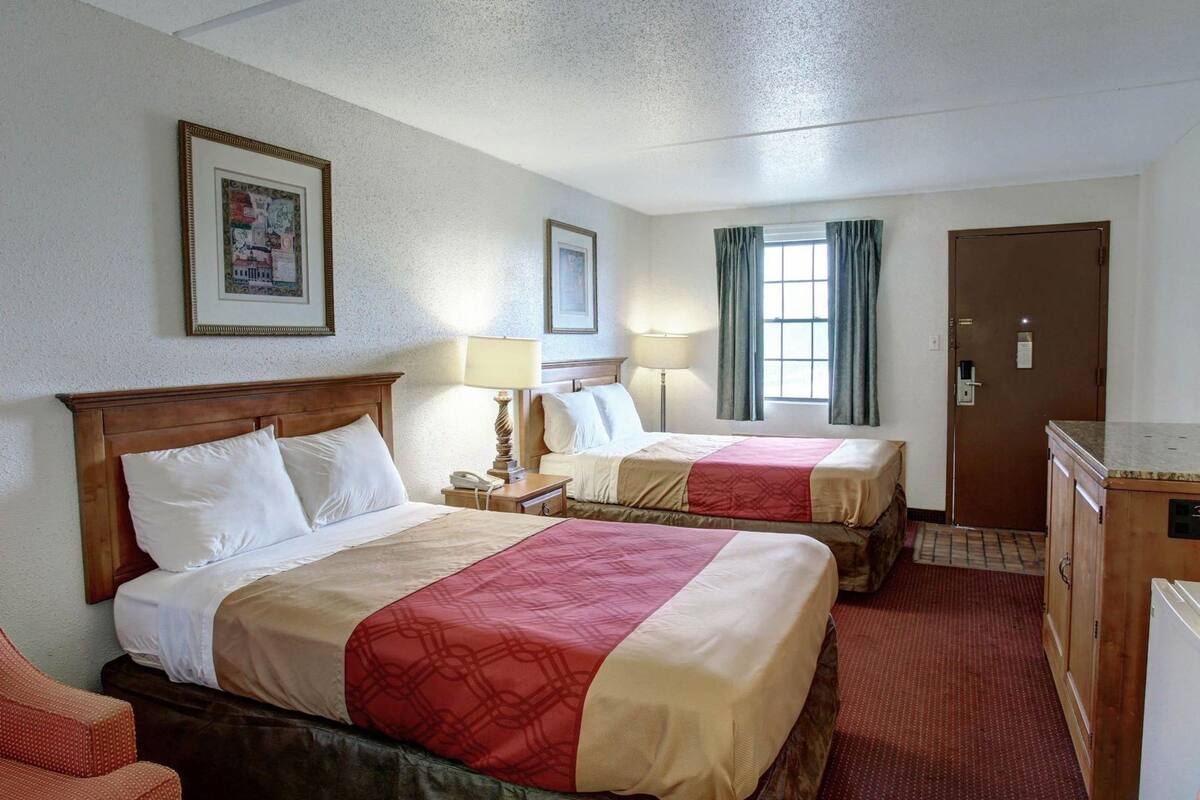 A hotel room with two beds, a desk, a chair, a dresser, and a door.